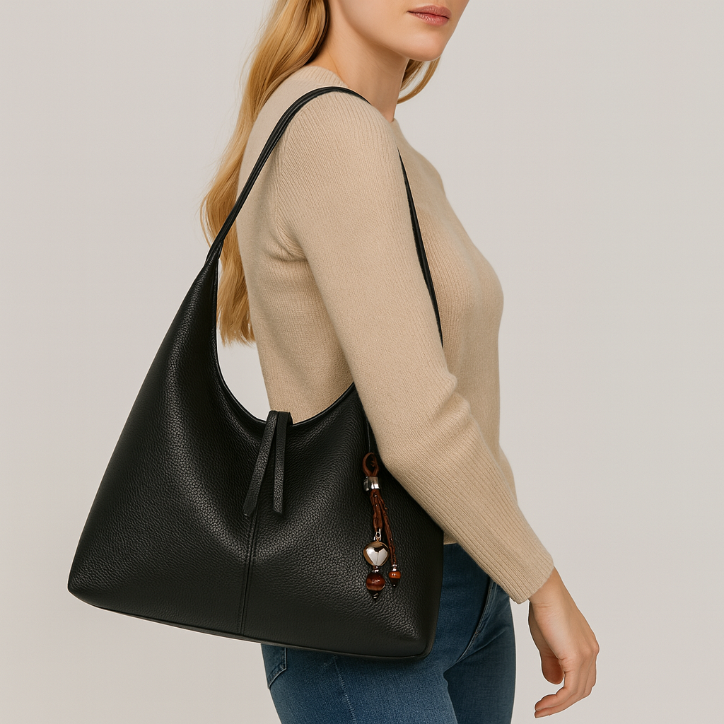 Minimalist slouchy shoulder bag with a single wide strap and decorative charm.